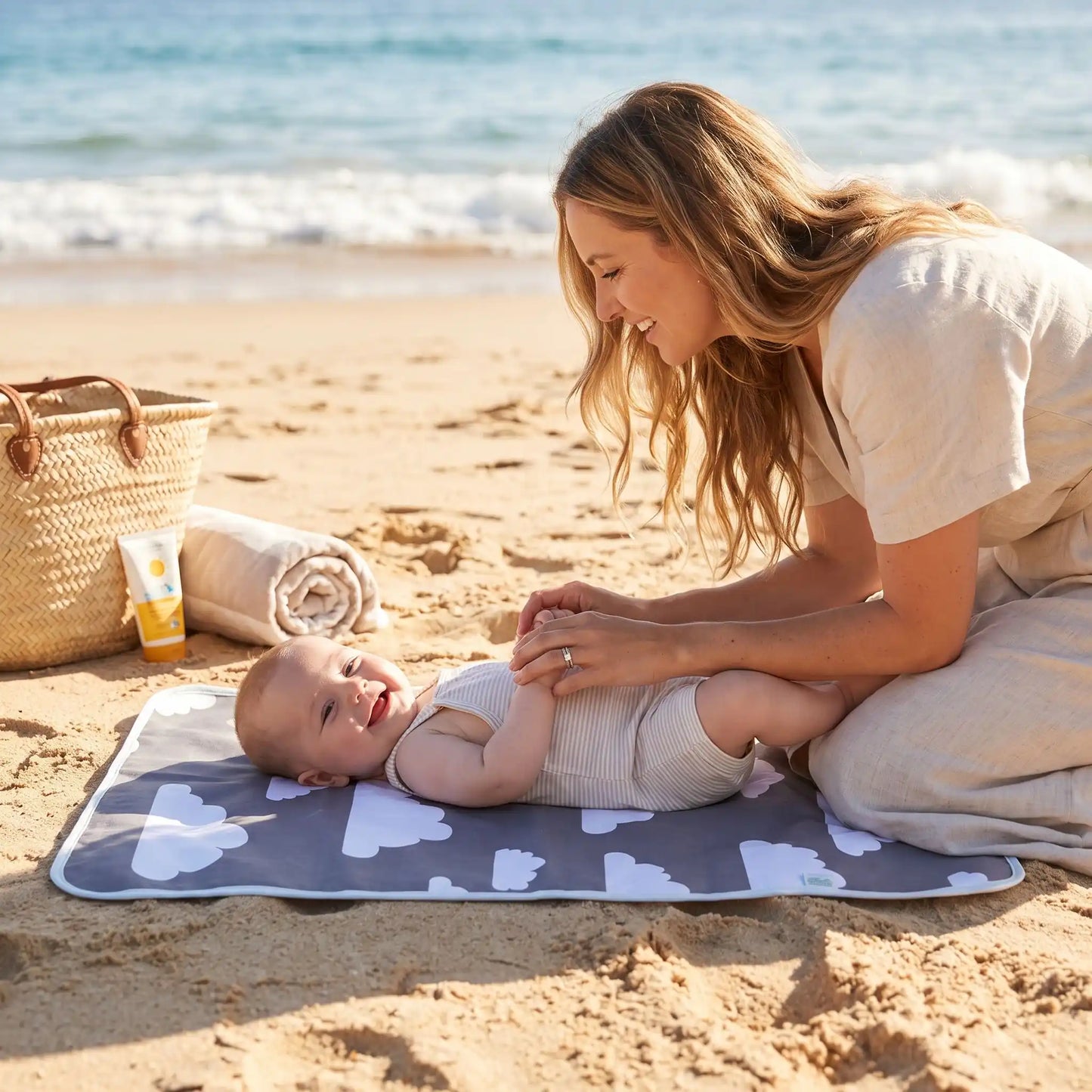bébé sur tapis à langer nuages à la plage avec maman