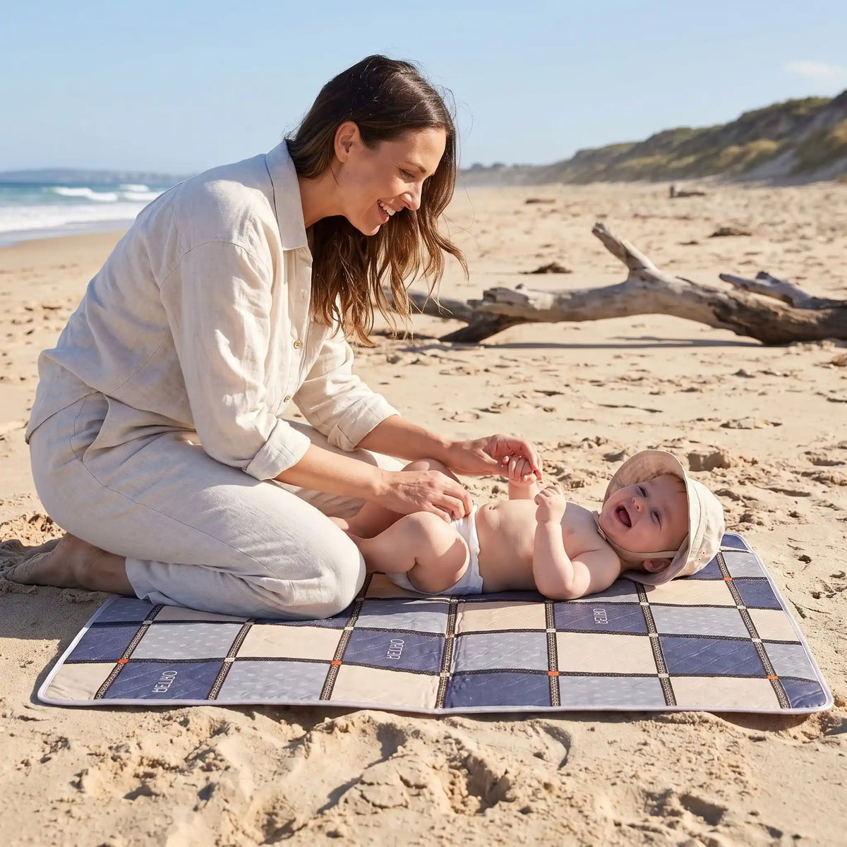 maman change bébé sur tapis langer voyage carreau sur la plage