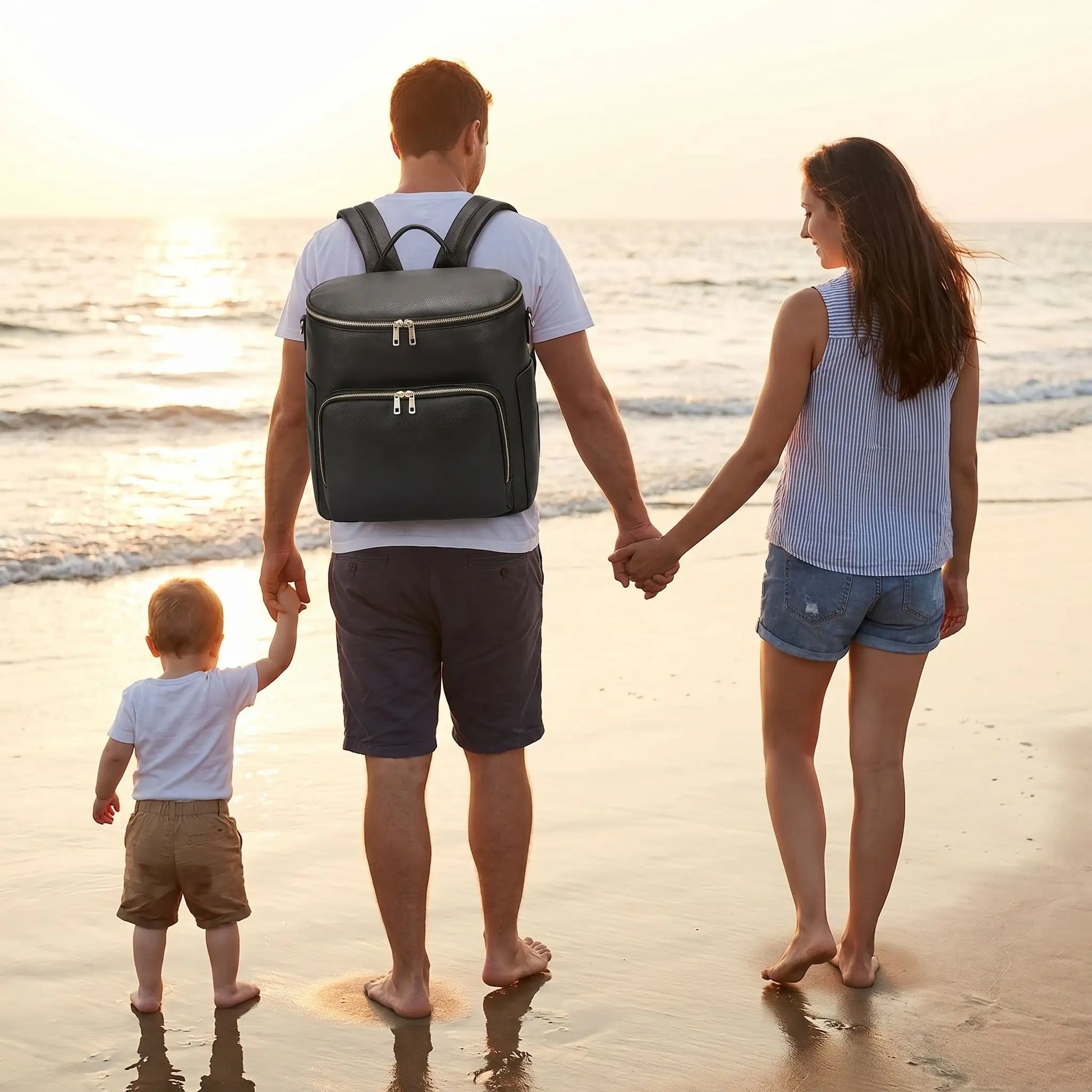 papa porte sac a langer chic cuir mompratique au dos  sur la plage avec bébé et maman